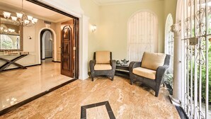A spacious foyer with a marble floor, a chandelier, wicker furniture, and a view through a decorative window. - Luxurious San Juan Villa w/ Pool - Walk to Beach! (San Juan)