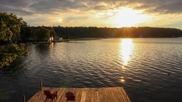 A wooden dock with two chairs, a calm lake, and a sunset in the background.