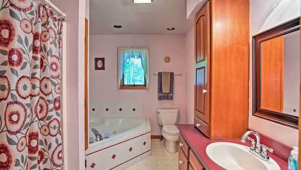A bathroom with a bathtub, toilet, sink, and wooden cabinets. - Lake Bonaparte 'fins & Feathers Lodge' w/ Dock! (Harrisville)