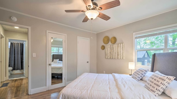 A bedroom with a large bed, a ceiling fan, a window with blinds, and a door leading to a bathroom.