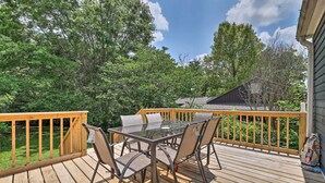 A wooden deck with a glass table and chairs, surrounded by a wooden railing and trees.