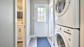 A laundry room with a front-loading washer and dryer, a white door, and a blue mat at the entrance.