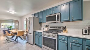 A modern kitchen with teal cabinets, stainless steel appliances, and a dining area with a table and chairs.