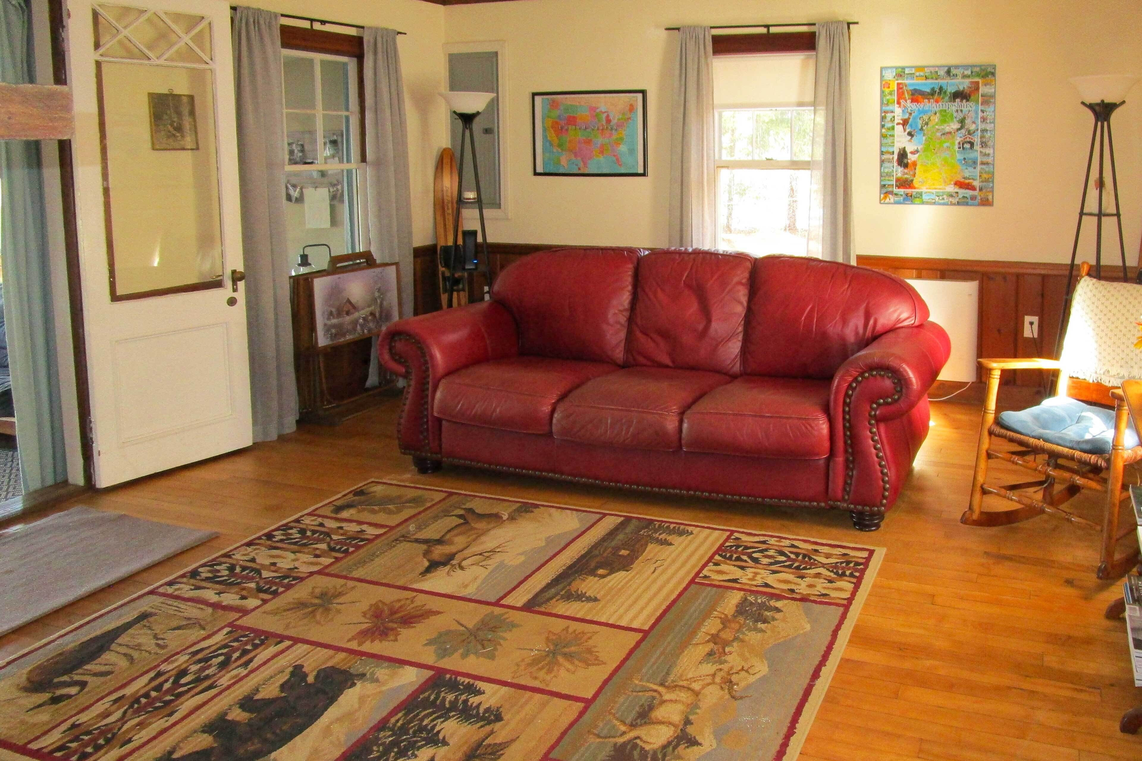 A living room with a red leather sofa, a patterned rug, wooden flooring, a wooden chair, and a lamp.
