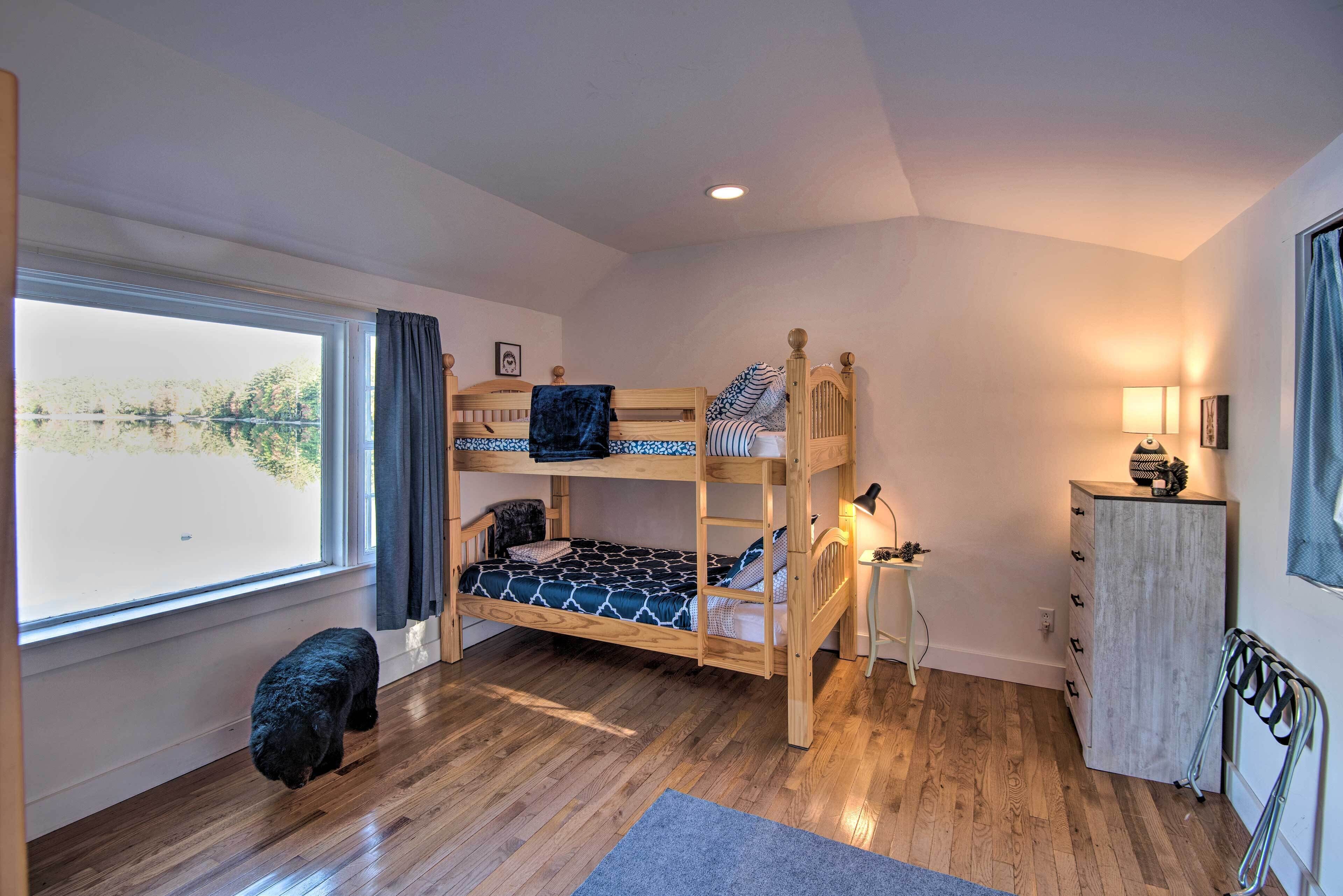 A room with a bunk bed, a desk, a chair, a lamp, and a view of the outdoors.
