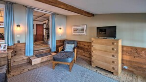 A cozy room with a wooden chair, a TV on a dresser, and a staircase leading to another area.