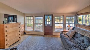 A cozy room with a wooden dresser, a leather sofa, and large windows offering a view of the outdoors.