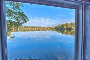Une vue d’un lac paisible, avec un quai et des arbres dont les reflets se mirent dans l’eau.