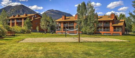 A hotel with a large outdoor area, including a hammock and a volleyball net, set against a backdrop of mountains and clear skies.