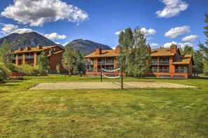 A hotel with a large outdoor area, including a hammock and a volleyball net, set against a backdrop of mountains and clear skies. - Walk to Main St: Frisco Condo w/ Community Pool! (Frisco)