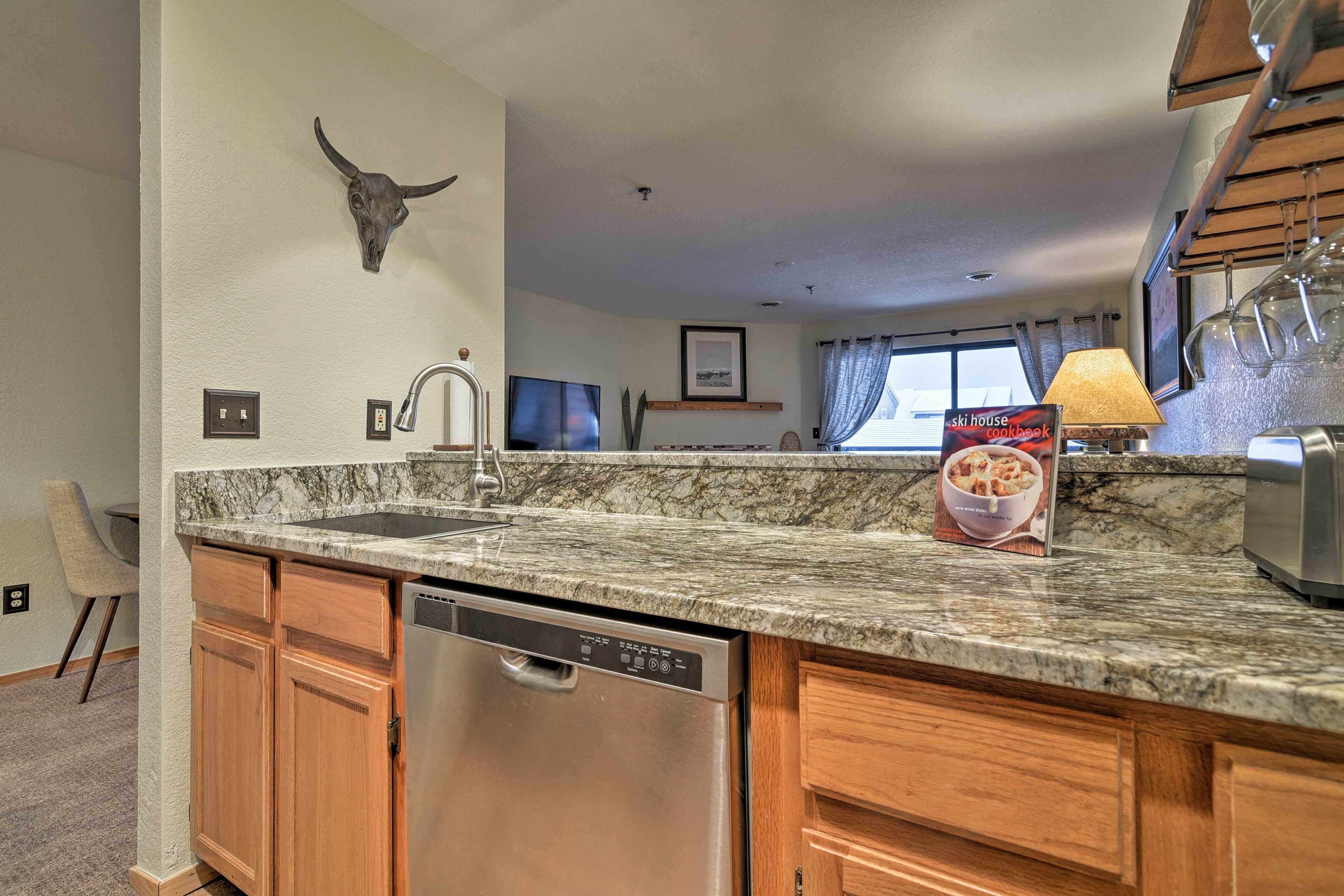 A kitchen with wooden cabinets, a stainless steel dishwasher, a marble countertop, a bull skull decoration, a television, and a cookbook on the counter.