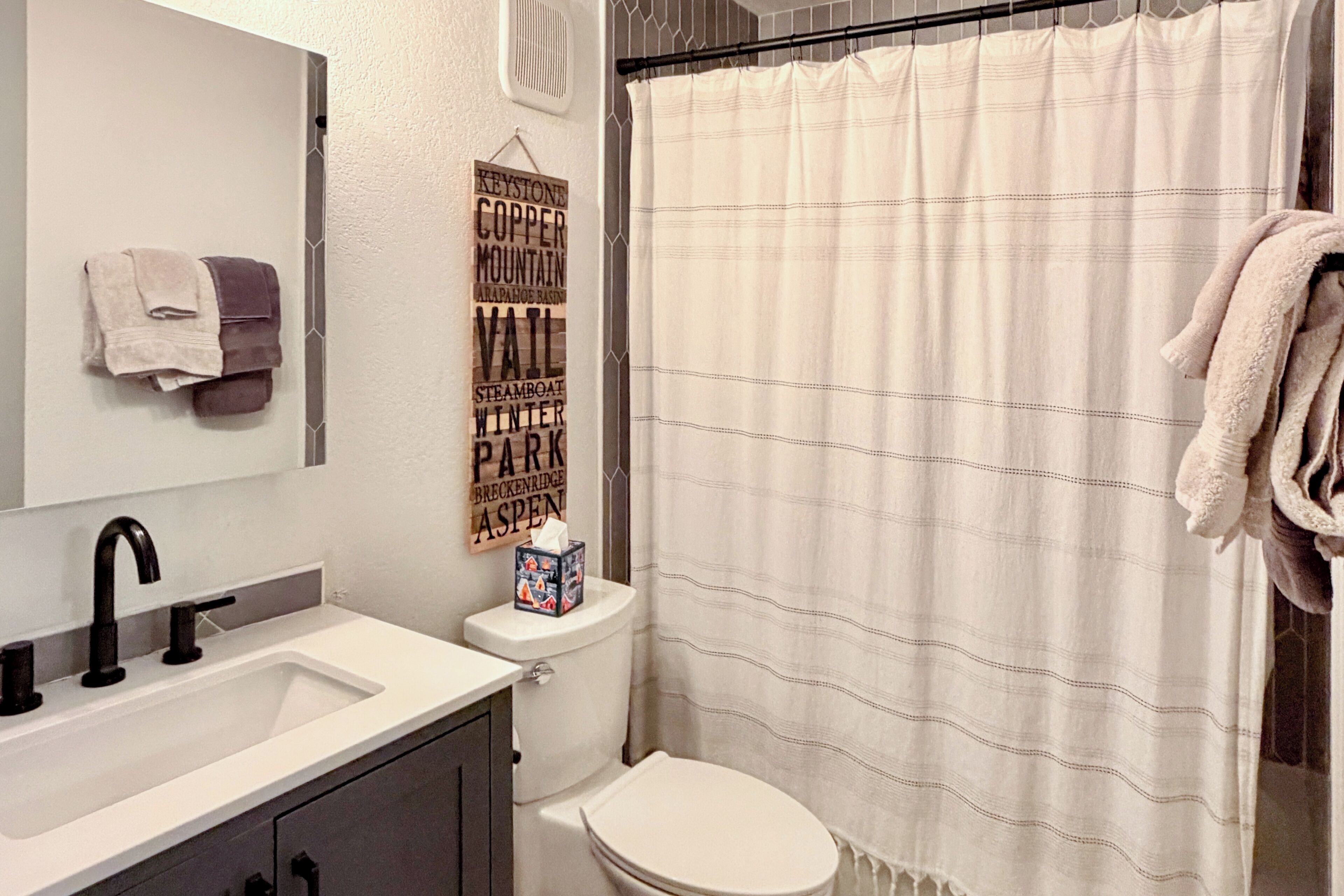 A bathroom with a white sink, black faucet, and a toilet. There is a shower curtain with a striped pattern. Towels are hanging on a rack.