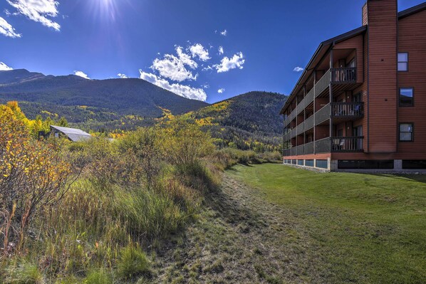 A modern building with multiple balconies, a grassy area, and a mountain backdrop. - Walk to Main St: Frisco Condo w/ Community Pool! (Frisco)