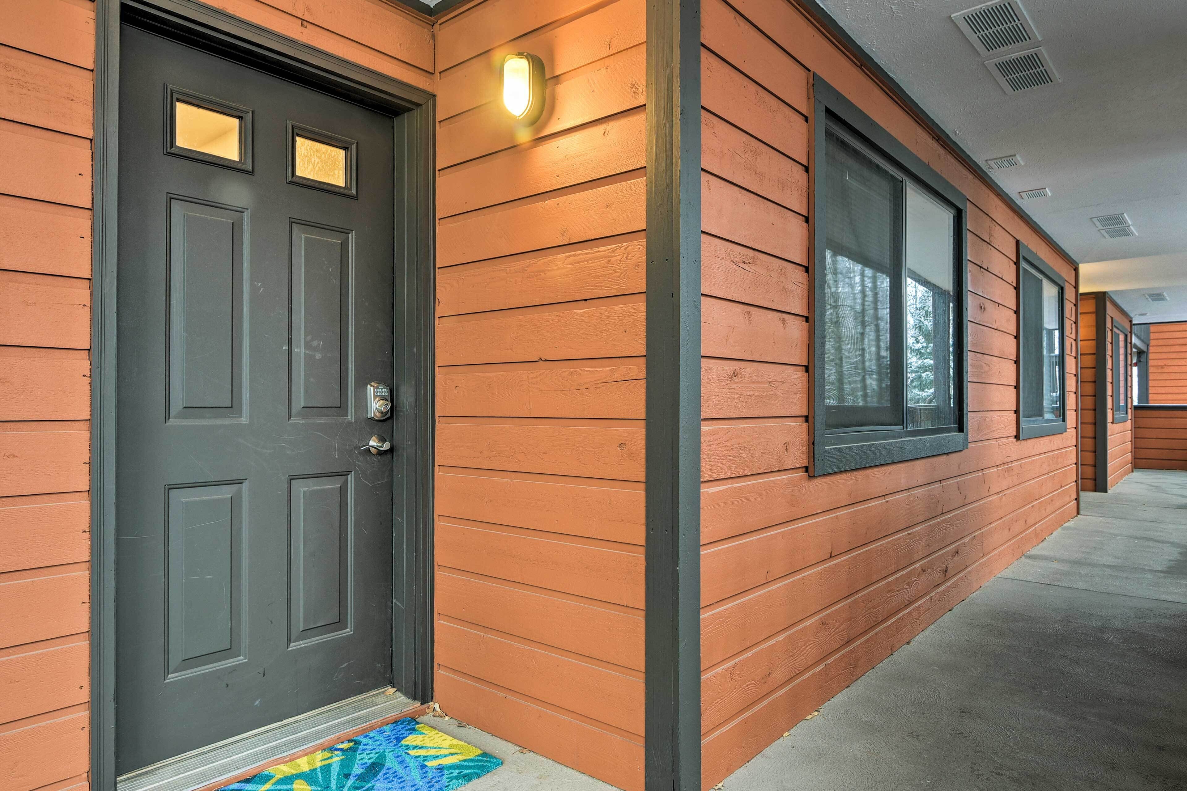 A building with a dark front door, wooden siding, and large windows.