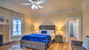 A bedroom with a large bed, two bedside lamps, a ceiling fan, a fireplace, and a view through a window. - Cozy Carpinteria Apartment: Walkable Location (Carpinteria)