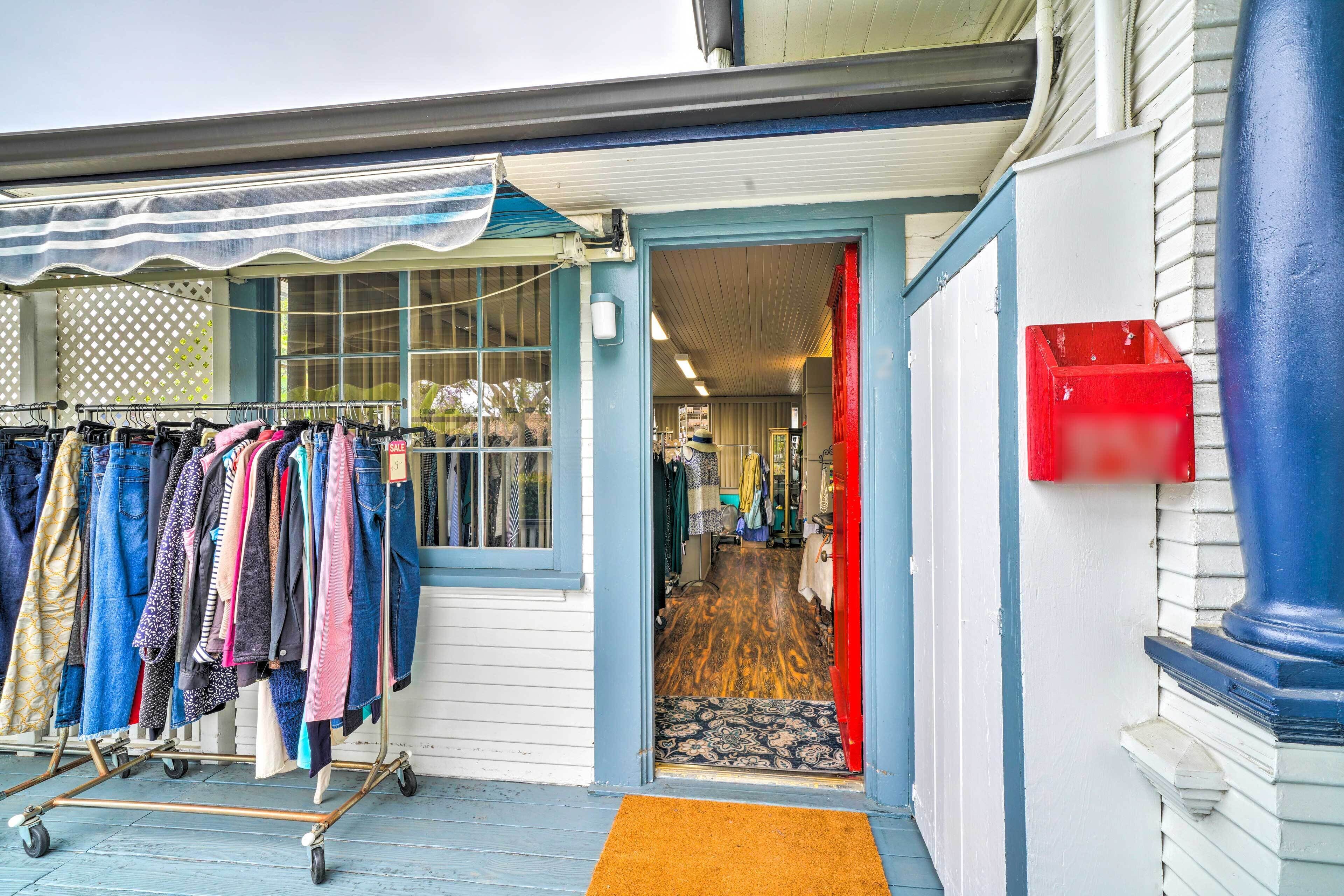 Une devanture de magasin avec un présentoir à vêtements à l’extérieur, une boîte aux lettres rouge et un tapis à motifs devant l’entrée.