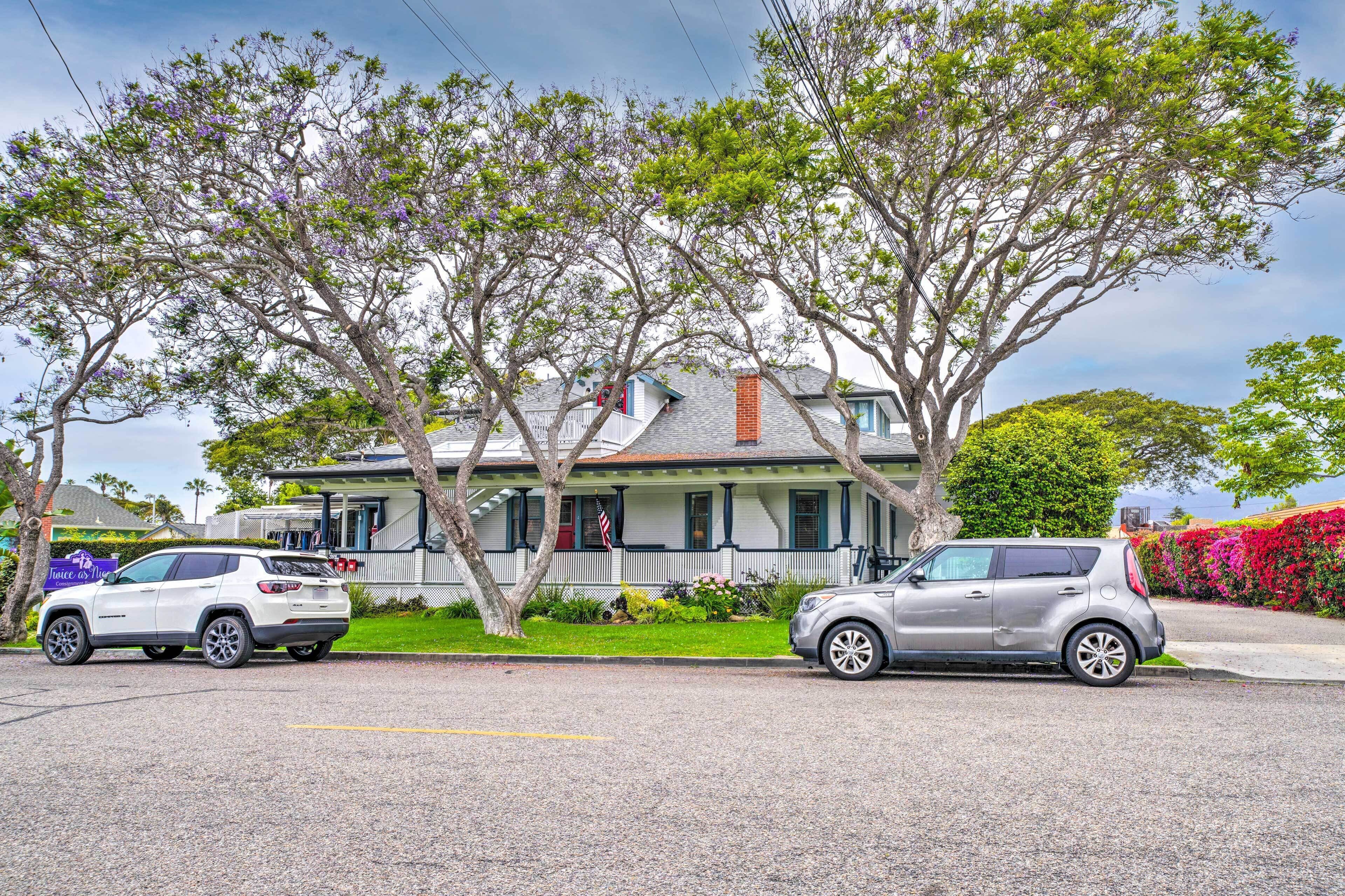 A two-story house with a porch, a small garden, and two parked cars.