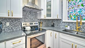 A modern kitchen with white cabinets, a black countertop, a stainless steel range hood, and a mosaic backsplash. - Cozy Carpinteria Apartment: Walkable Location (Carpinteria)