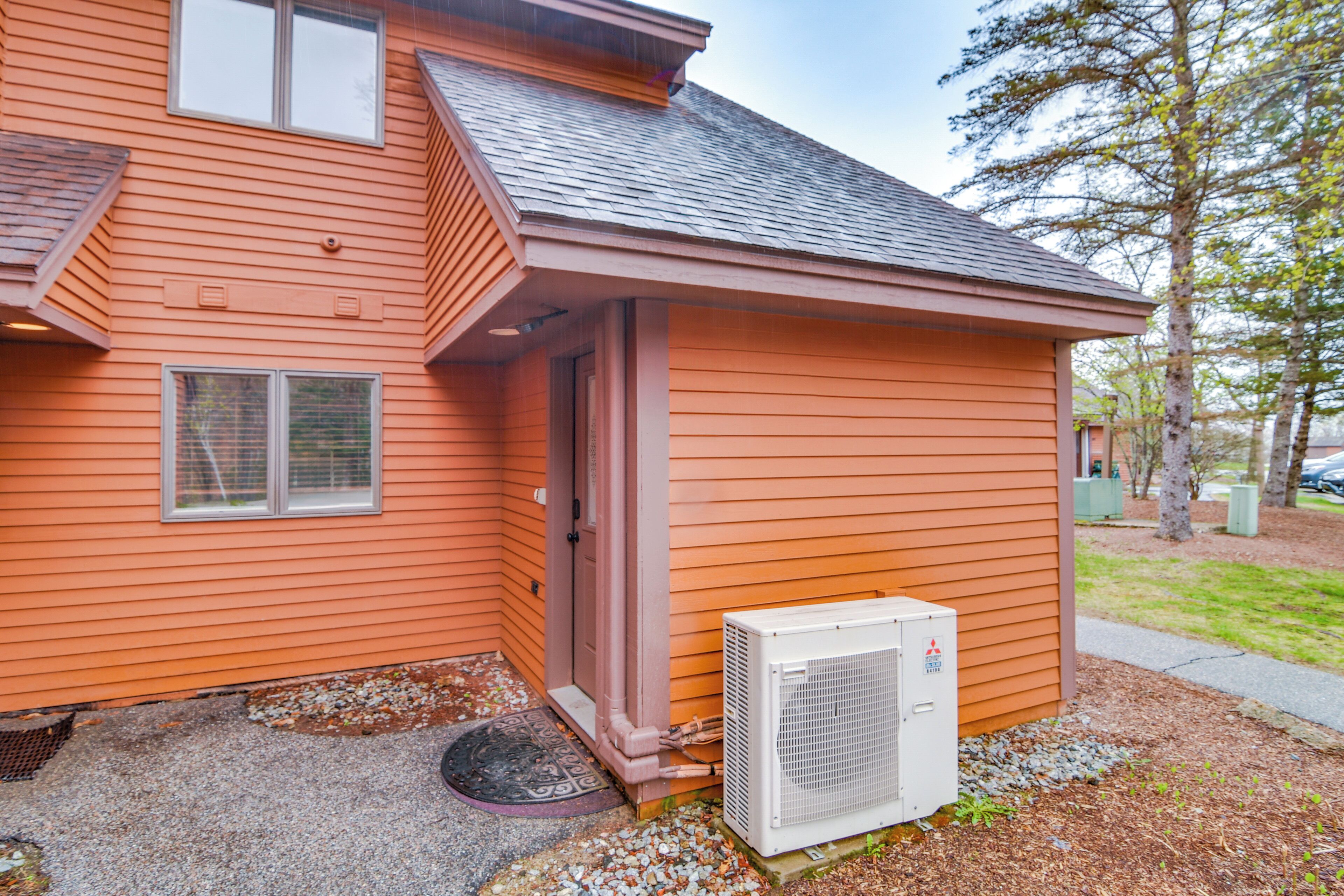 A house with a small attached garage, a door, and an air conditioning unit.