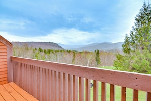 Une terrasse en bois offrant une vue sur un paysage boisé et des montagnes à l’horizon.