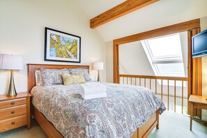 Une chambre à coucher avec un grand lit, une tête de lit en bois, un puits de lumière, une télévision et une table de chevet avec une lampe.
