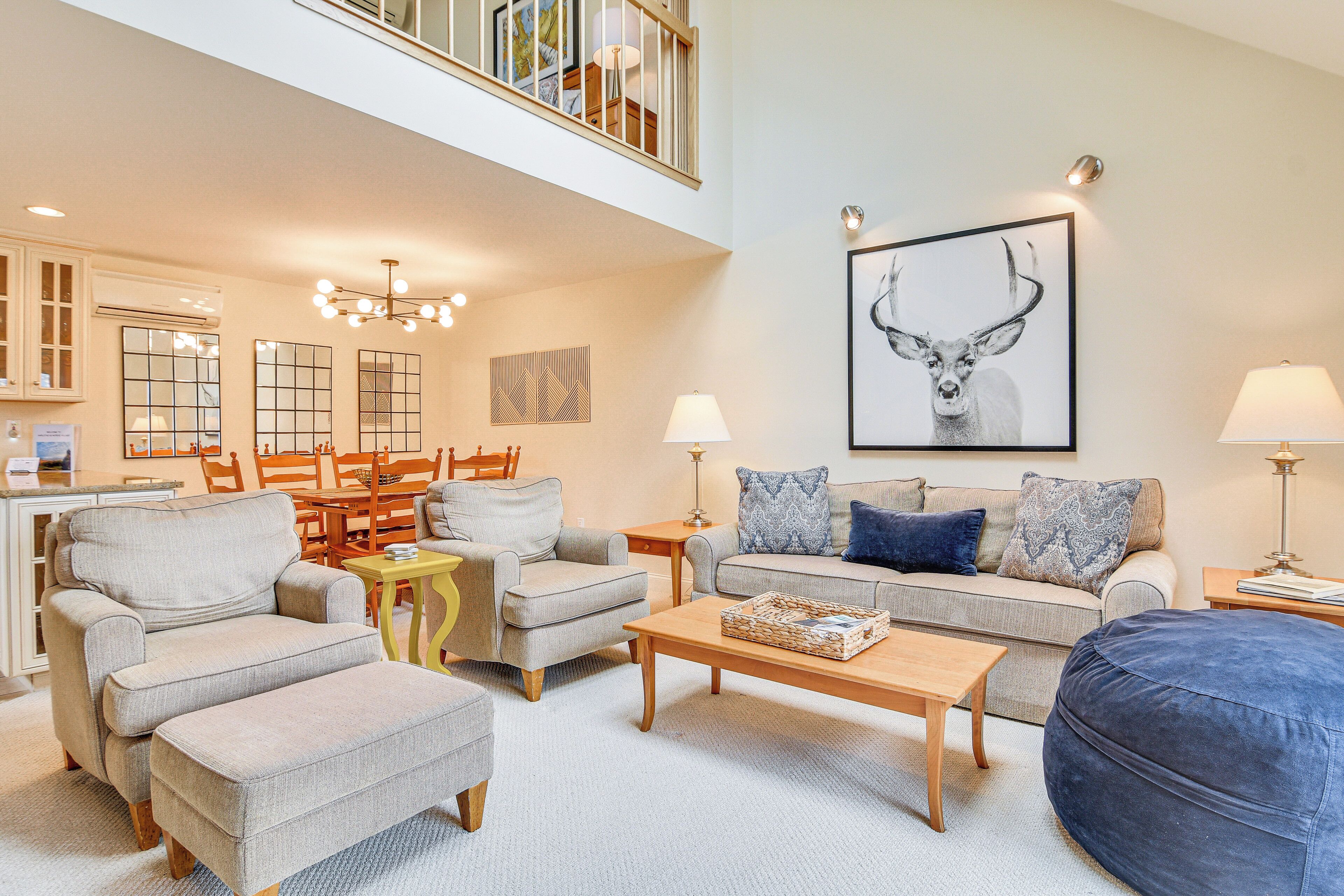 A spacious living room with a high ceiling, a dining area with wooden furniture, and a large framed deer artwork on the wall.