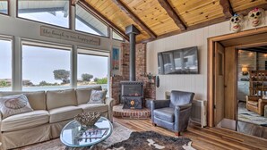 A cozy living room with a fireplace, leather furniture, and large windows overlooking a scenic view. - Irish Beach Cottage w/ Beach Access & Ocean Views (Manchester)