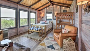 A cozy cabin-style room with a bed, a leather chair, a wooden bench, and a view of the outdoors through large windows. - Irish Beach Cottage w/ Beach Access & Ocean Views (Manchester)