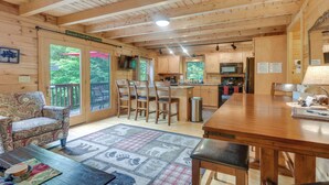 A wooden cabin interior with a dining area, kitchen, and a large window overlooking greenery. - Updated Log Cabin Near Story Land & Diana's Baths! (Conway)