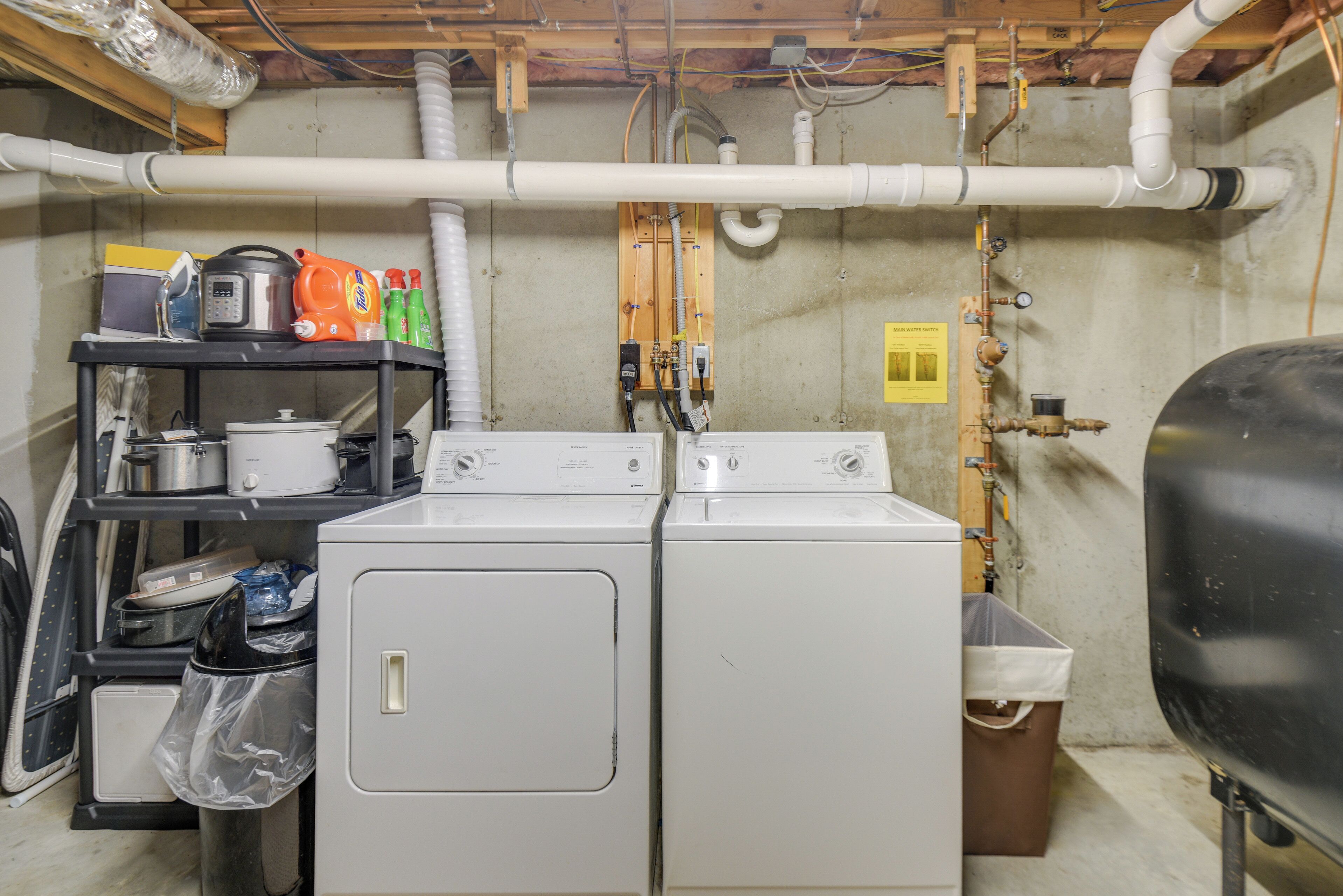 A laundry area with two stacked washers and dryers, a shelf with cleaning supplies, and a grill.