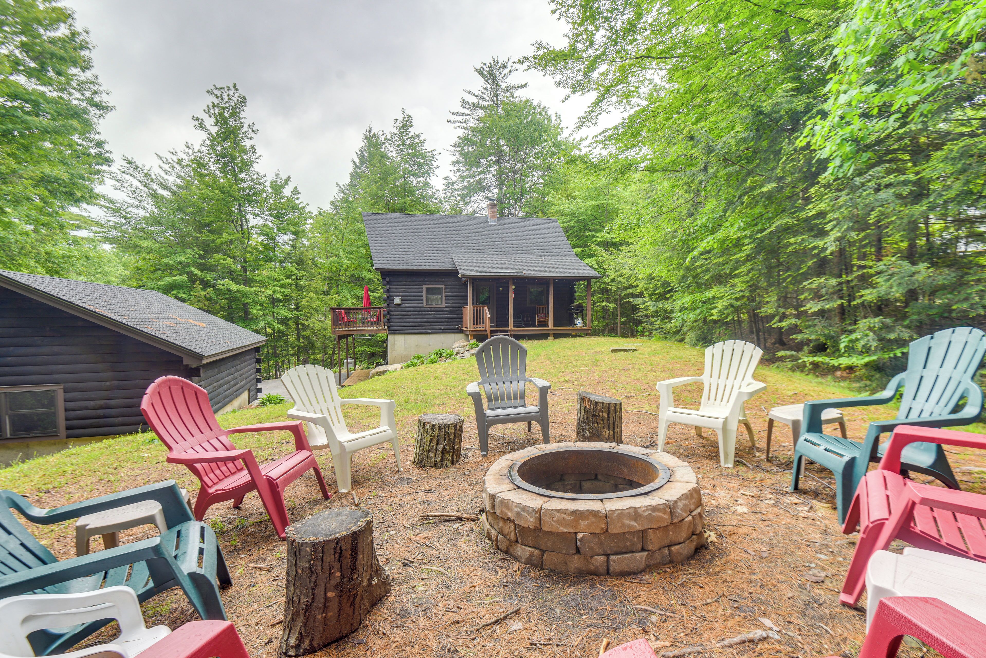 A cabin with a fire pit and Adirondack chairs in a forest setting.