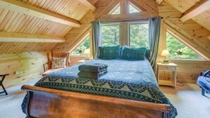 A bedroom with a wooden ceiling, a bed with patterned bedding, a nightstand, and a window with curtains. - Updated Log Cabin Near Story Land & Diana's Baths! (Conway)