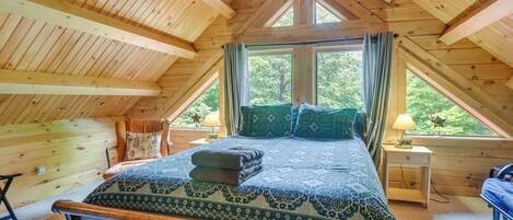 Un dormitorio con techo de madera, una cama con ropa de cama estampada, una mesita de noche y una ventana con cortinas.