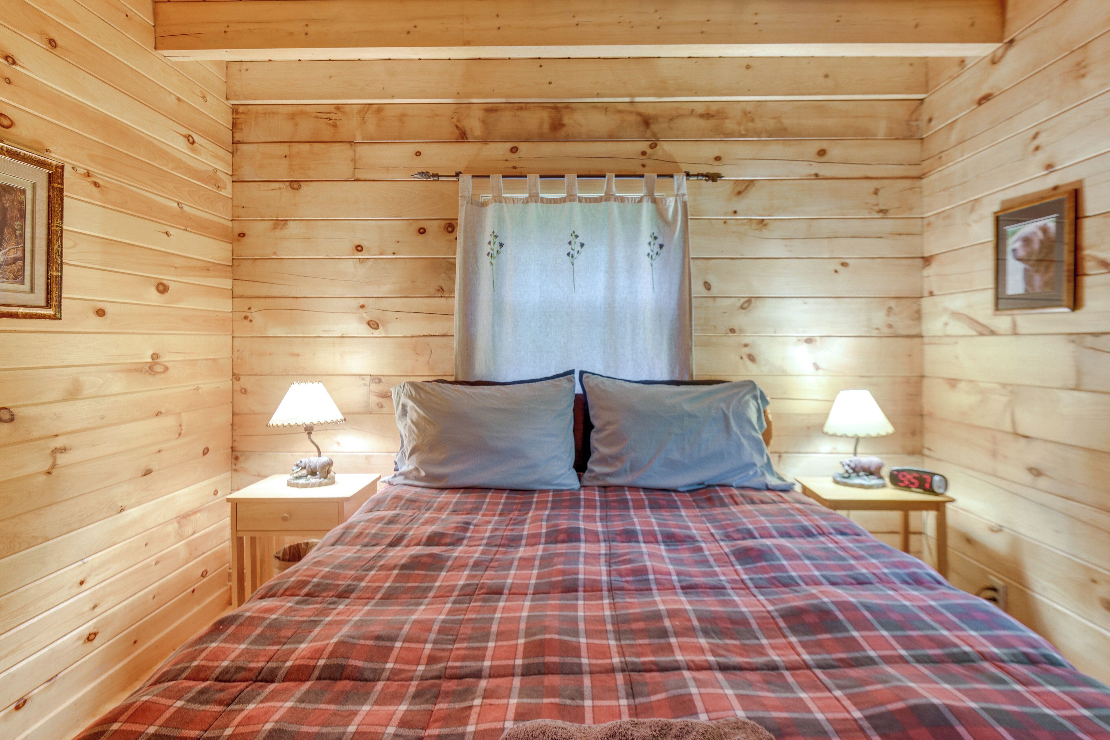 Ein Schlafzimmer einer Holzhütte mit einer Karo-Bettdecke, zwei Nachttischlampen, einer Uhr und einem gerahmten Bild an der Wand.