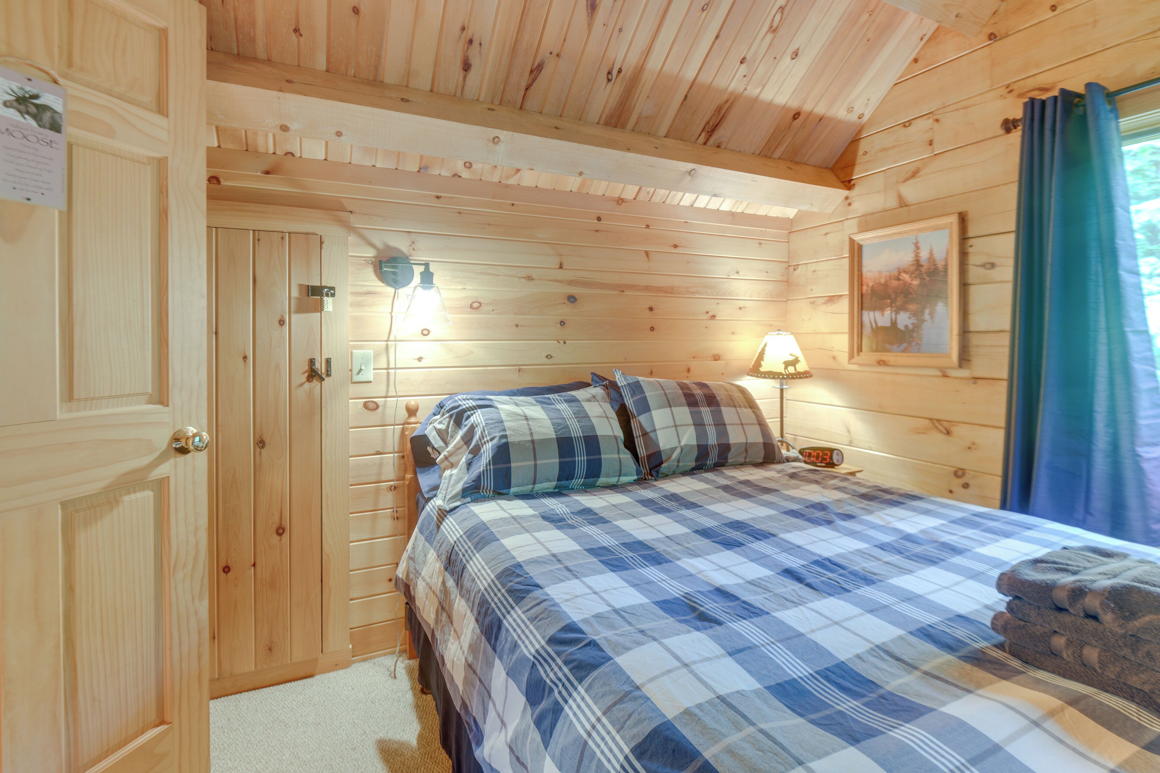 A wooden cabin room with a bed, a nightstand, a lamp, and a painting on the wall.