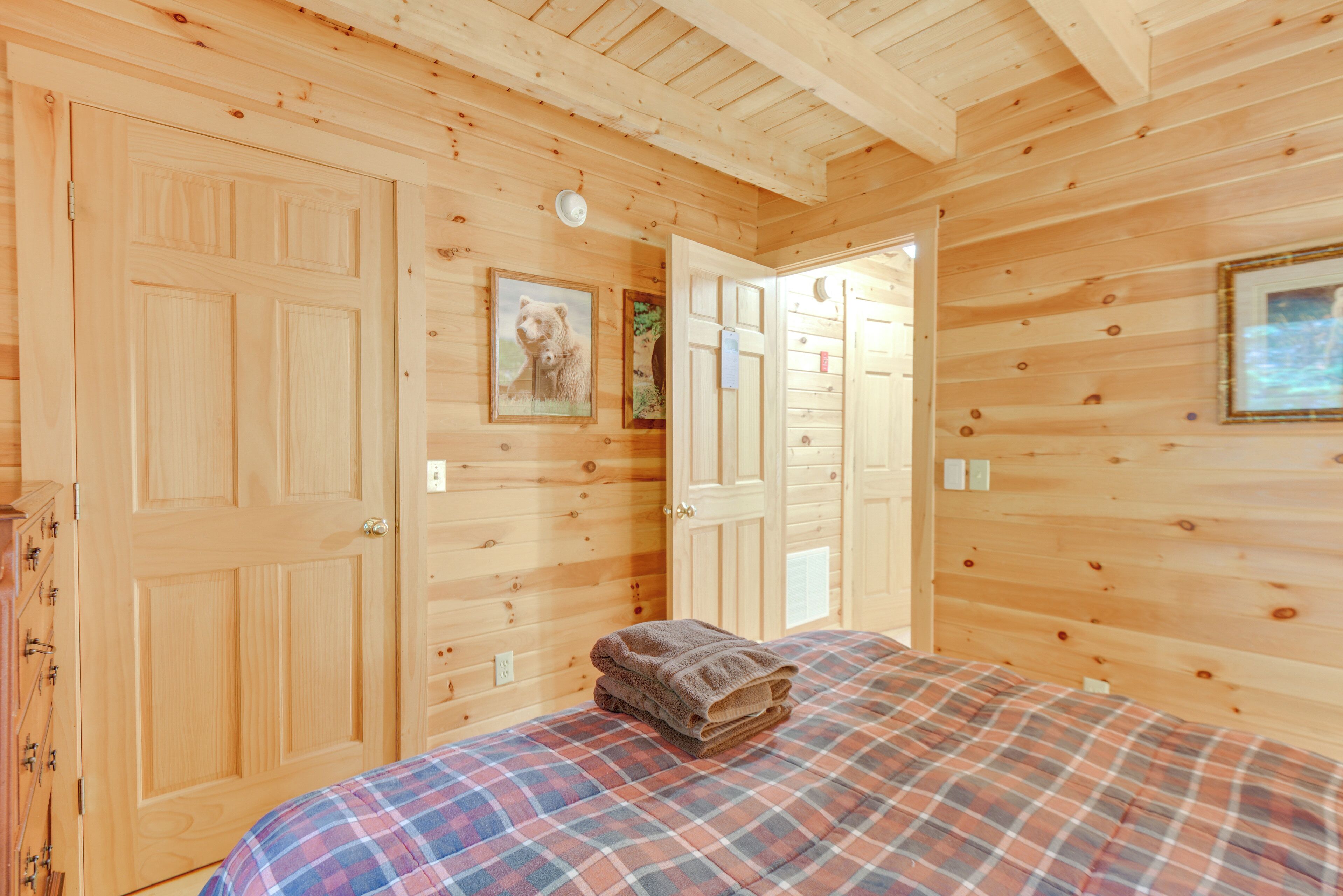 A wooden cabin room with a bed, a door, and a wall-mounted picture.
