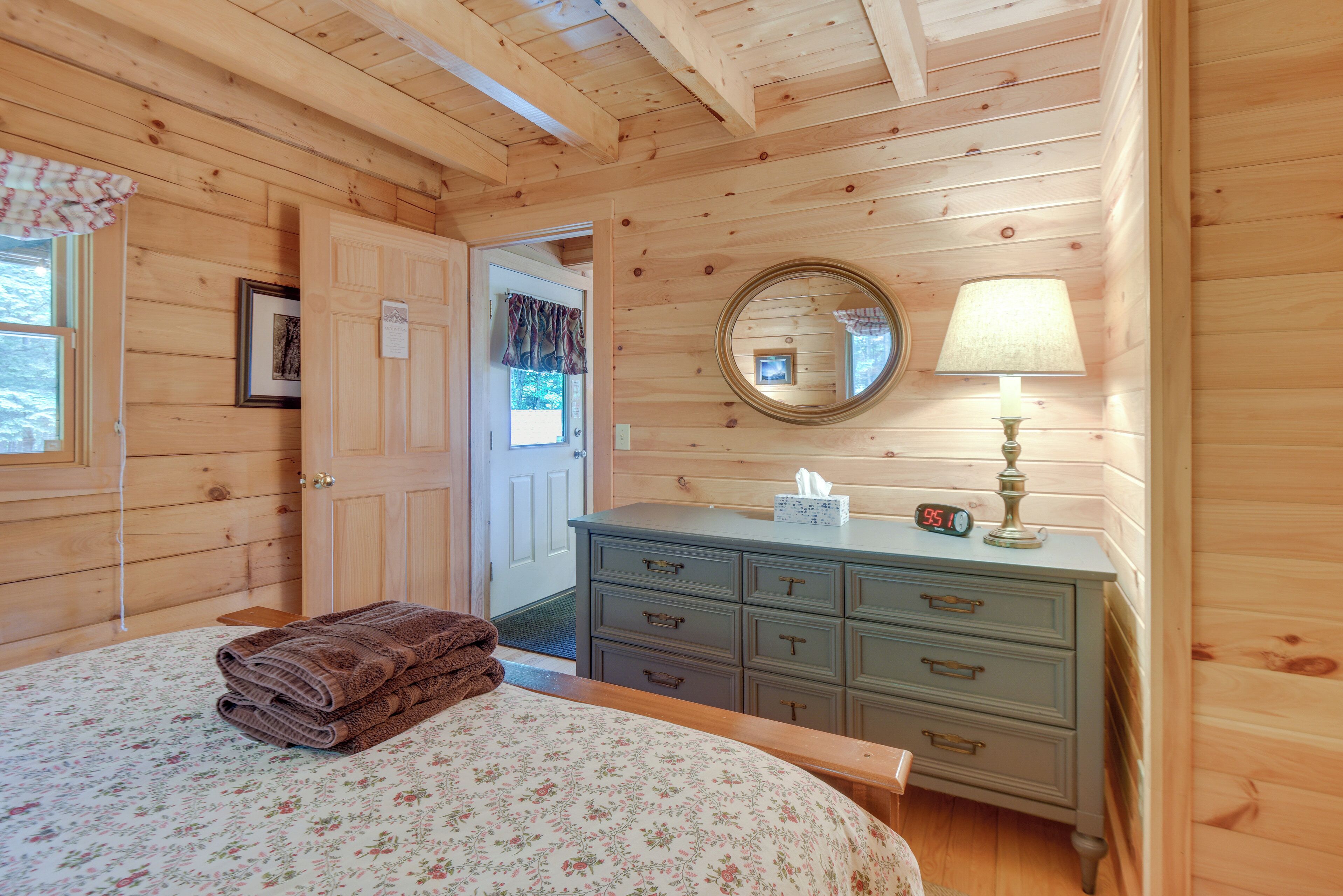 A wooden cabin bedroom with a bed, dresser, mirror, and a clock.