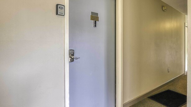 Un pasillo con una puerta, un detector de incendios y un felpudo.