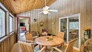A wooden interior with a round wooden table and chairs, a ceiling fan, and a view through a glass door to an outdoor area.