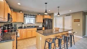 A modern kitchen with wooden cabinets, a central island with bar stools, stainless steel appliances, and pendant lighting.
