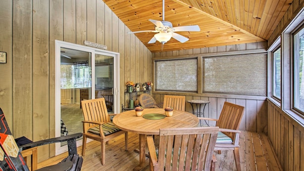 A wooden interior with a round table and chairs, a ceiling fan, and large windows.
