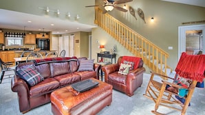 A spacious living room with a leather sofa, a rocking chair, and a staircase leading to a second floor.