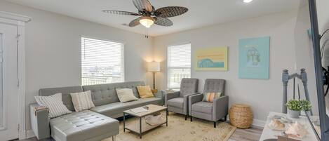 A living room with a grey sofa, two armchairs, a coffee table, a ceiling fan, and a television.