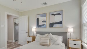 Ein Schlafzimmer mit einem Bett, zwei Nachttischen, einer Kommode und abstrakter Wandkunst.