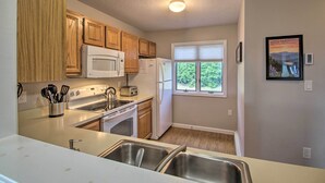 A kitchen with wooden cabinets, a microwave, a refrigerator, a stove, and a window with a view of greenery. - Intervale Family Retreat: Mtn View & Pool Access! (Intervale)