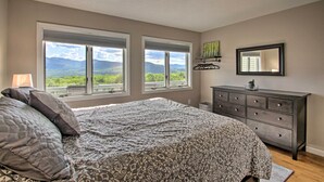 A bedroom with a large bed, two windows with a mountain view, a dresser, and a mirror. - Intervale Family Retreat: Mtn View & Pool Access! (Intervale)