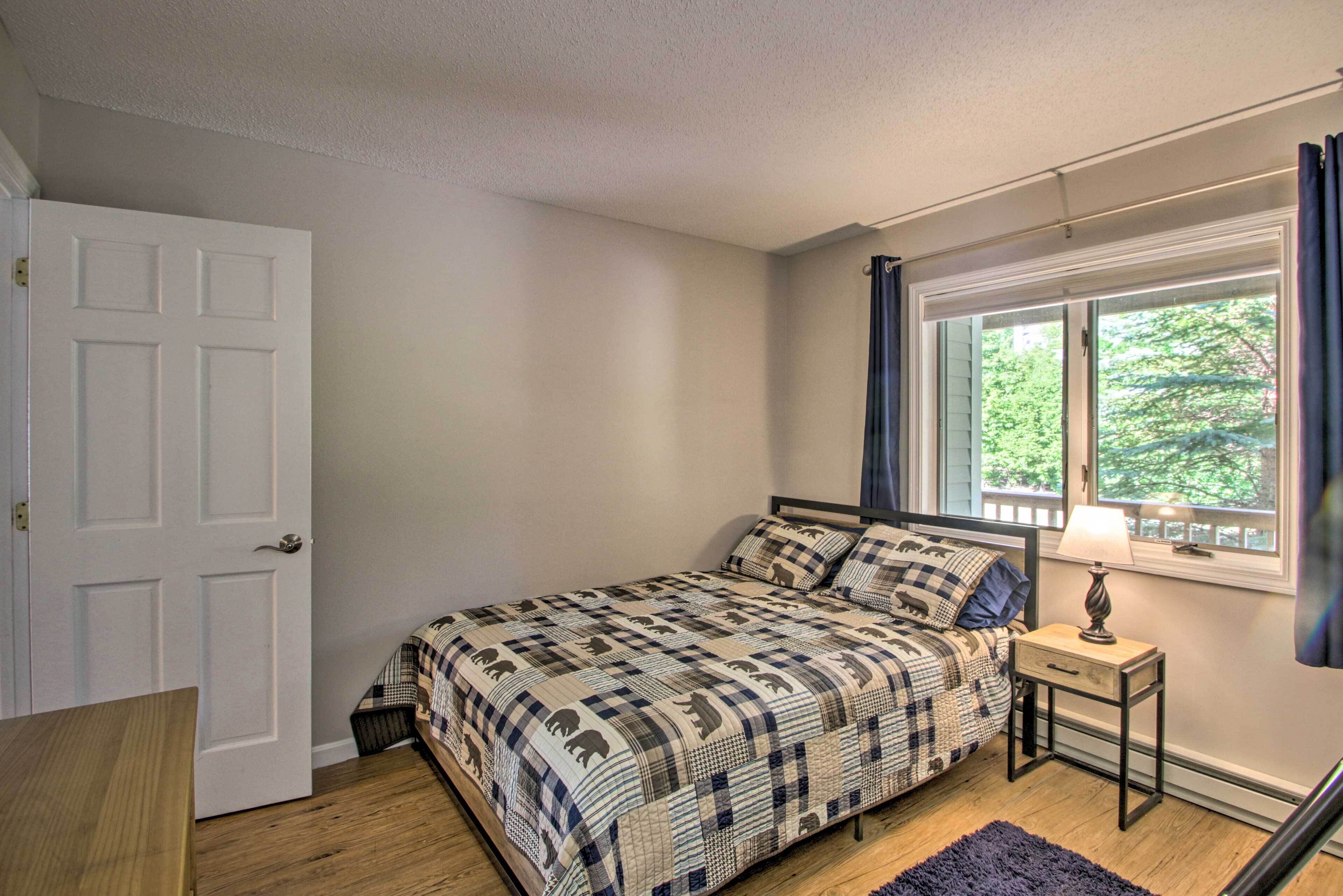 A bedroom with a bed, a nightstand, a window with curtains, and a door.