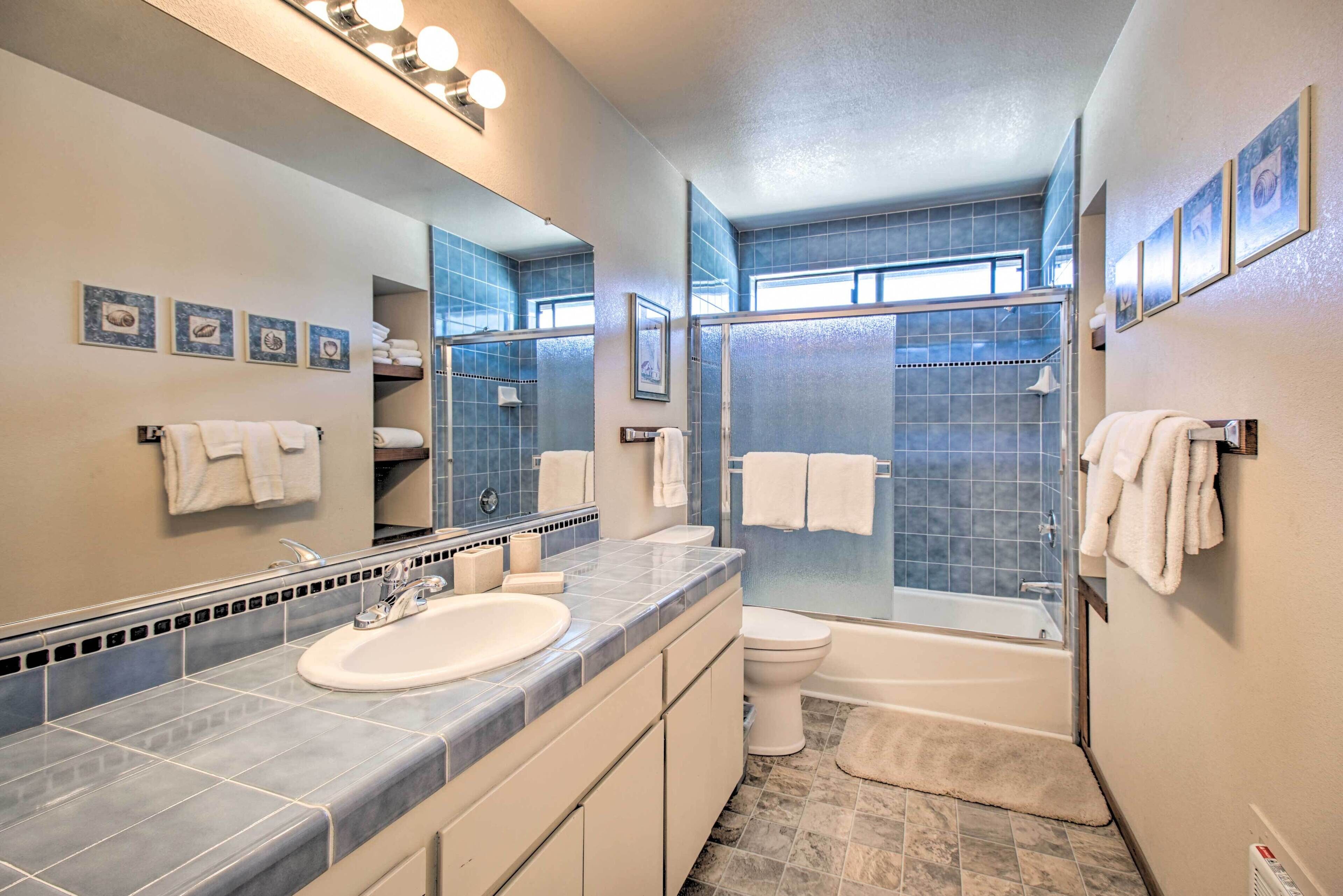 A modern bathroom with a large mirror, two sinks, a toilet, and a bathtub.
