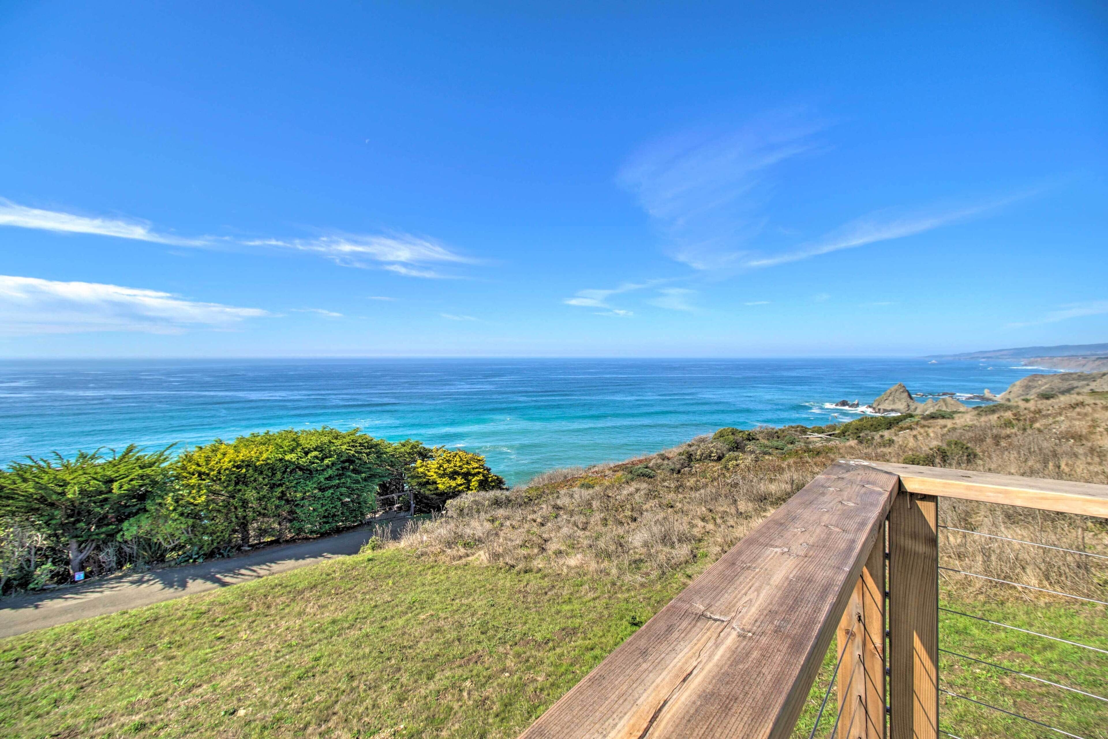 A coastal view with a wooden railing, grassy terrain, and the ocean.
