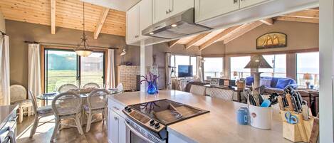 A spacious kitchen with a large island, wooden ceiling beams, and a view of the outdoors.